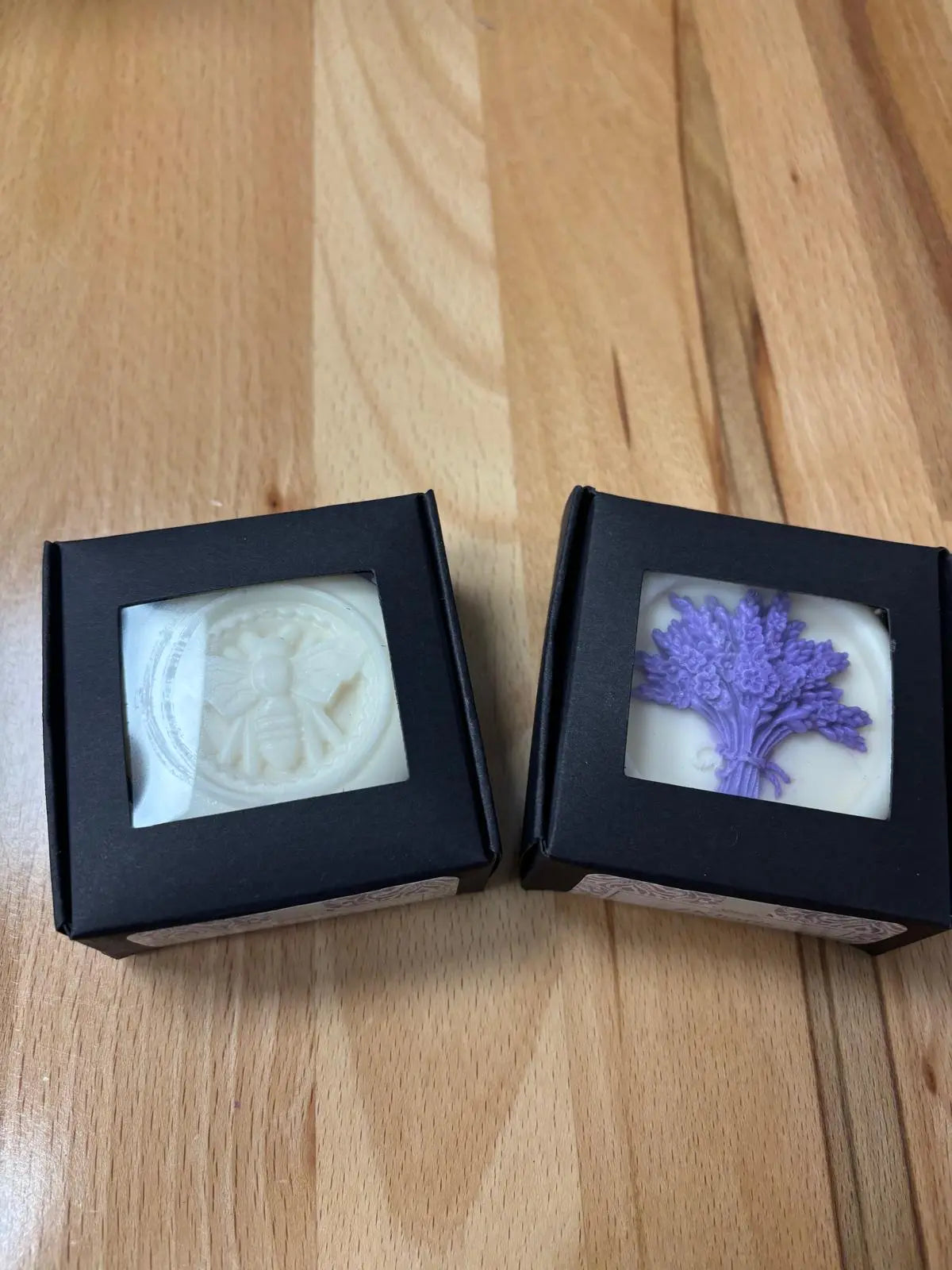 Two soap bars in black boxes on a wooden surface